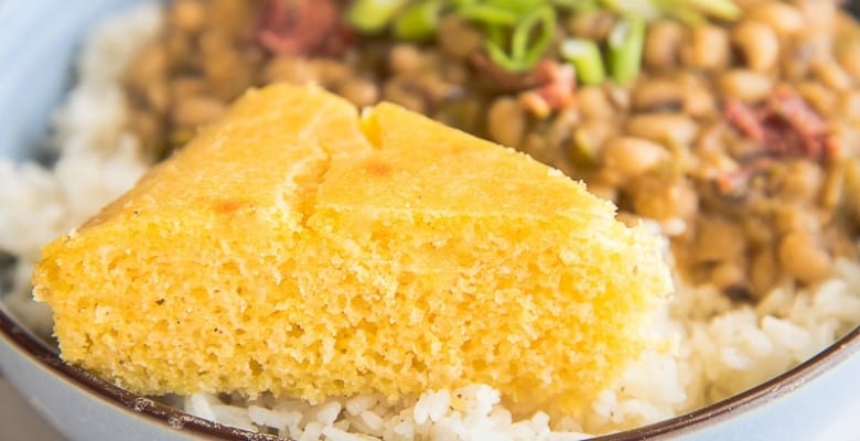 A close up image of a slice of cornbread on a pile of white rice in a light blue bowl