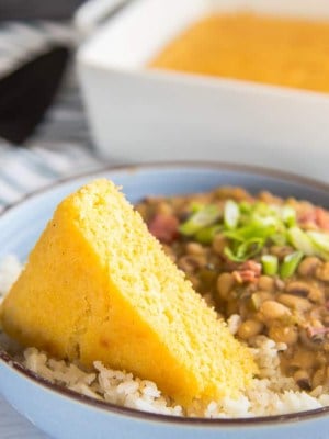 horizontal image of a blue bowl with a brown rim filled with rice, pease and a triangle slice of yellow cornbread