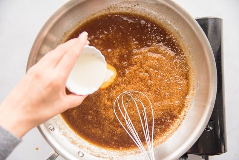 Cream added to caramel in a silver pan with a whisk.