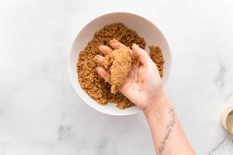 A hand holds a clump of oatmeal cookie crust to show it is properly mixed.