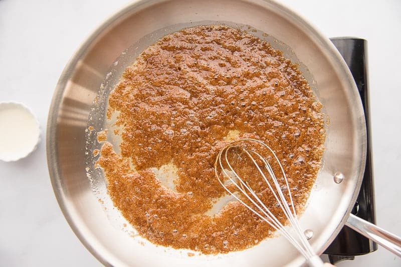 A whisk combines brown sugar and butter in silver sauté pan.