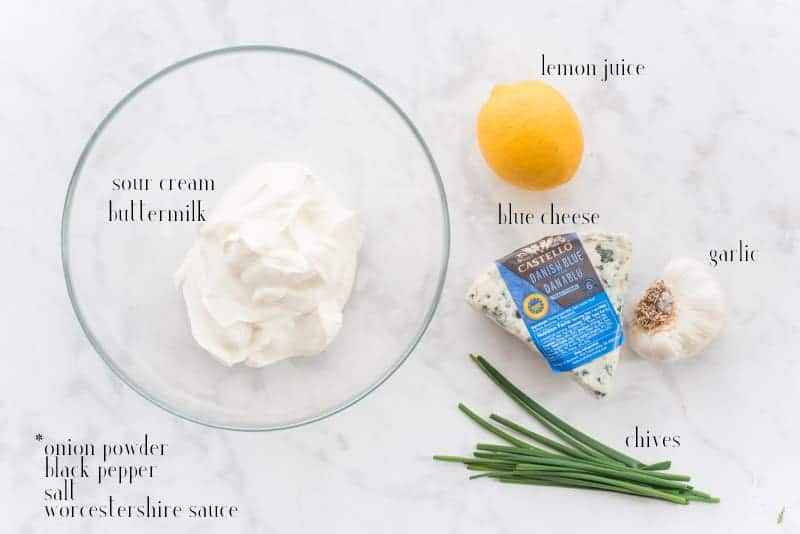 Ingredients for Blue Cheese dressing are shown: sour cream, buttermilk, a lemon, blue cheese, garlic, chives. Black text overlay of unshown ingredients reads: onion powder, black pepper, salt, worcestershire sauce