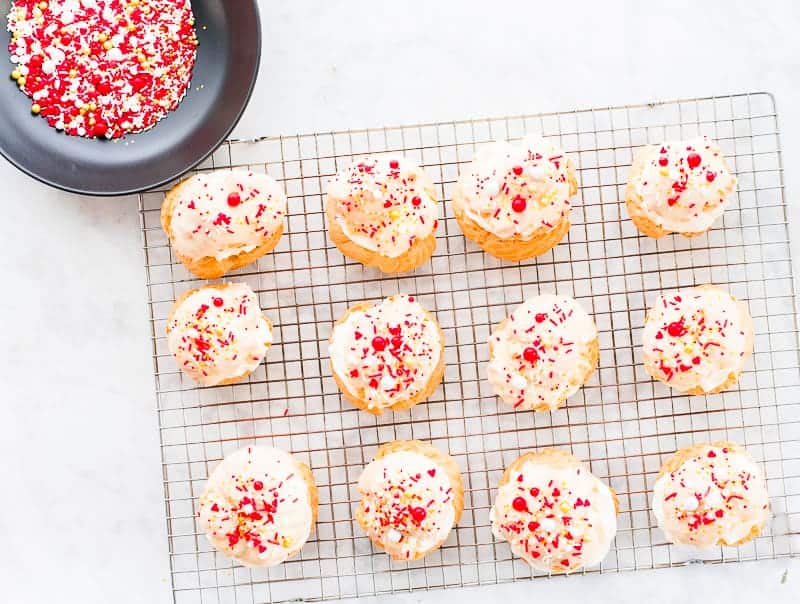 A cooling rack with 12 cream puffs sprinkled with Valentine's sprinkles