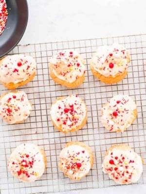A silver cooling rack with 12 Cream Puffs decorated with white chocolate ganache and Valentine's sprinkles.