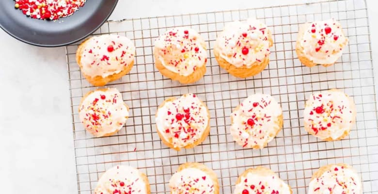 A silver cooling rack with 12 Cream Puffs decorated with white chocolate ganache and Valentine's sprinkles.