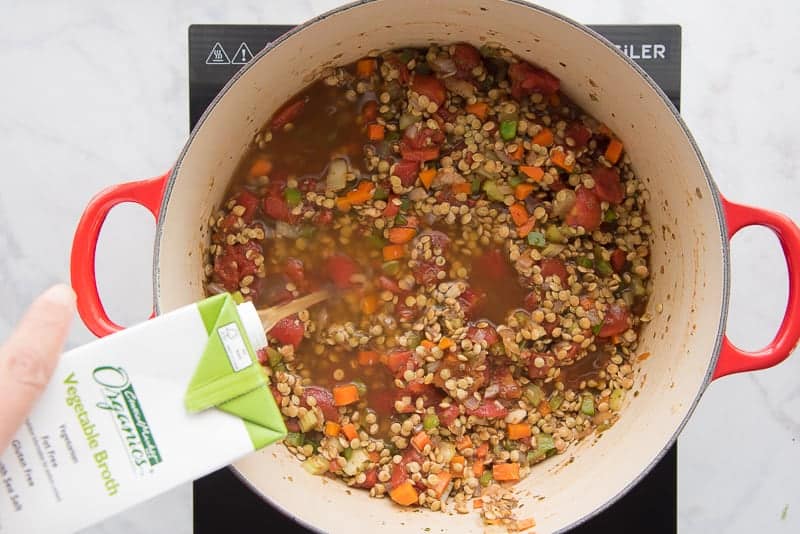 Vegetable broth pouring into a pot of lentils and veggies.