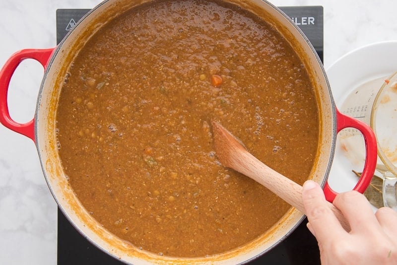 A wooden spoon stirring Vegan Lentil Stew in a red Dutch oven