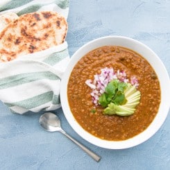 Overhead landscape image white bowl vegan lentil soup. Green and white towel with naan on a blue surface