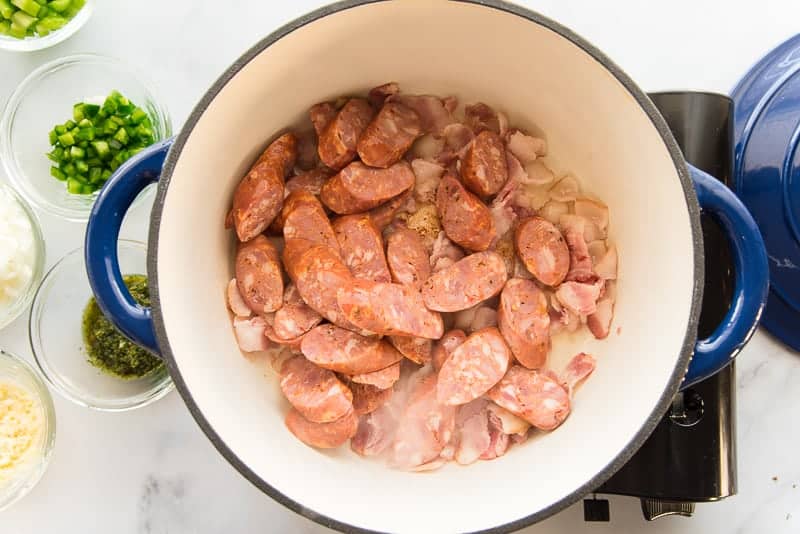 Andouille sausage and bacon are browned in a blue pot