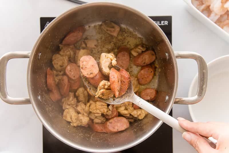 The chicken and sausage are browned in a silver pot.