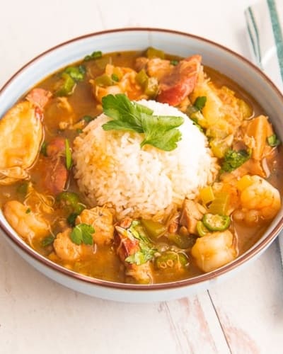 Close-up horizontal image blue bowl white rice gumbo, green and white striped napkin, black spoon on top, tabasco bottle