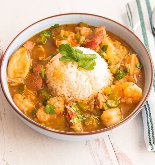 Close-up horizontal image blue bowl white rice gumbo, green and white striped napkin, black spoon on top, tabasco bottle