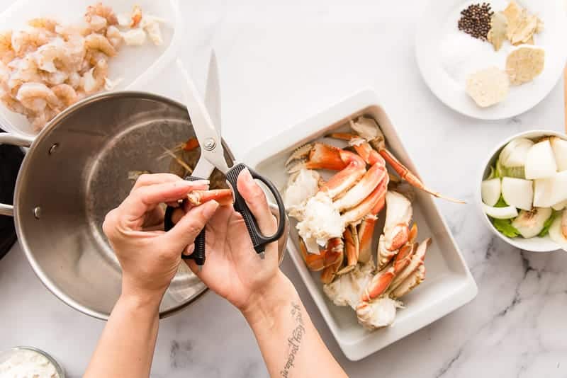 A hand uses kitchen shears to split the shell of a crab leg to extract the meat.
