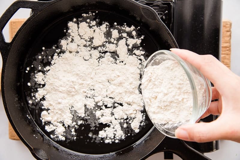 Flour is sprinkled into the melted lard in a cast iron skillet
