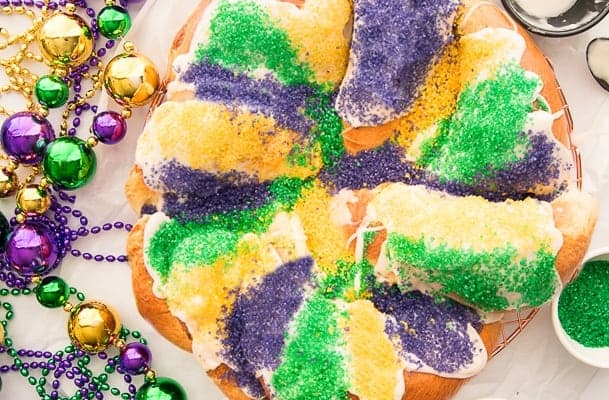 Overhead image of a sugared King Cake surrounded by beads and sanding sugar.