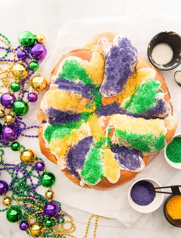 Overhead image of a sugared King Cake surrounded by beads and sanding sugar.