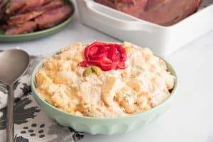 horizontal image green bowl of Puerto Rican potato salad with red pepper garnish on top