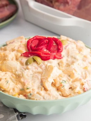 horizontal image green bowl of Puerto Rican potato salad with red pepper garnish on top