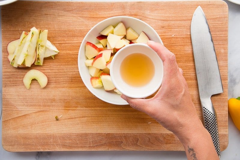 Apple cider vinegar in a white bowl held over a large white bowl filled with chopped apples