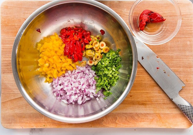 diced bell peppers, olives, cilantro, and red onion in a silver mixing bowl