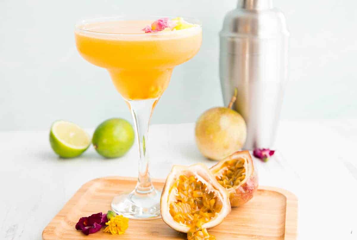 Preview image of a clear coupe glass of Classic Passion Fruit Daiquiri on a wooden plate with a half of a passion fruit split open.