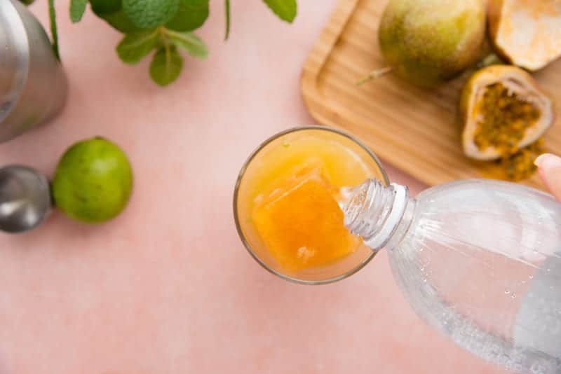 Seltzer water is poured over the Passion Fruit Mojito Mix in a clear glass