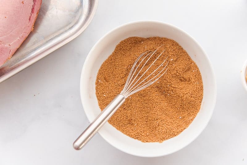 The spice blend is combined with a whisk in a white bowl.