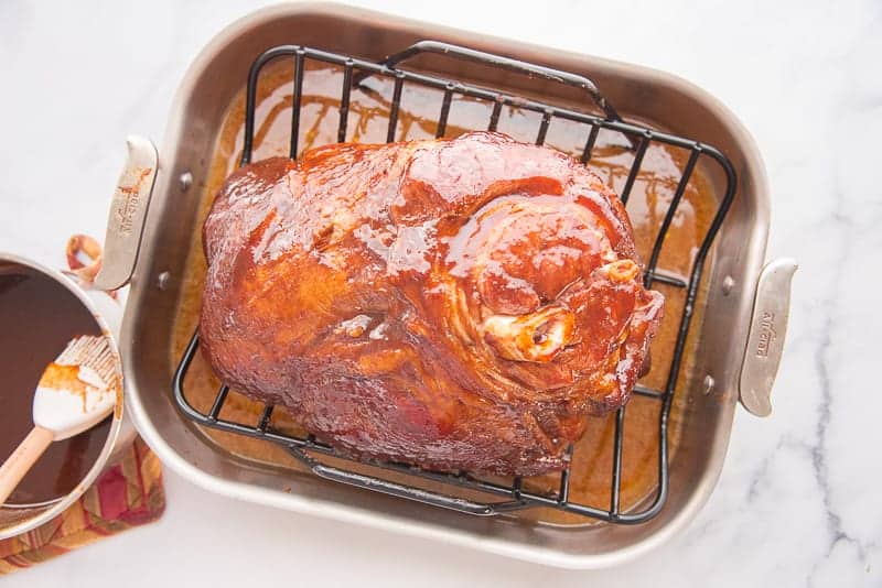 The ham is brushed with the spiced brown sugar pineapple glaze on a black rack in a metal roasting pan