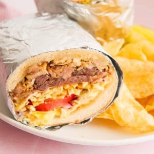 Up close image of the cut Tripleta wrapped in foil on a white plate next to potato chips
