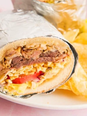 Up close image of the cut Tripleta wrapped in foil on a white plate next to potato chips
