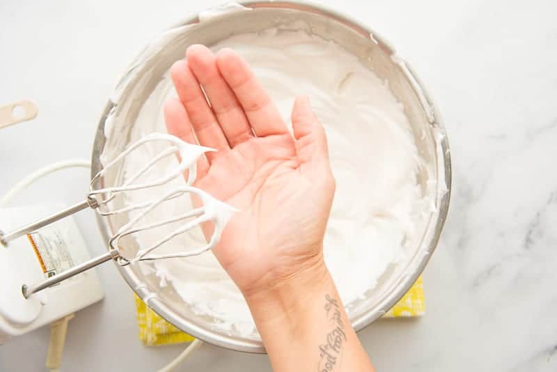A hand under whipped egg whites to show stiff peak consistency.