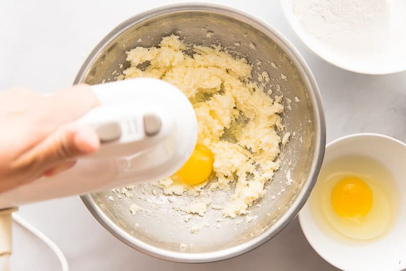 Butter, sugar, and eggs are creamed together with a hand mixer in a silver bowl.