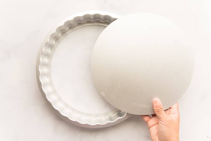 A hand lifts the false bottom from a quiche pan.