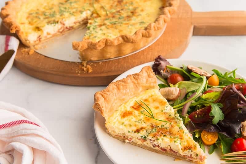 Horizontal image of a slice of Quiche Lorraine on a white plate next to a garden salad