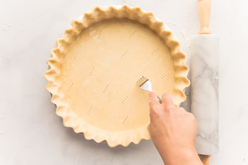 A hand uses a fork to poke holes into a shell of pie dough