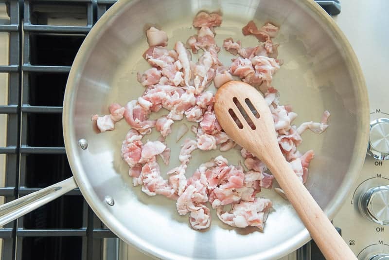 Chopped bacon in a skillet with a wooden spoon prior to cooking.
