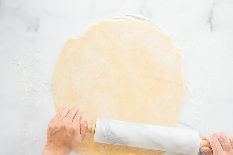 Hands using a marble rolling pin to roll out pie dough