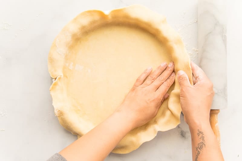 Hands pressing pie dough into a pie tin marble rolling pin
