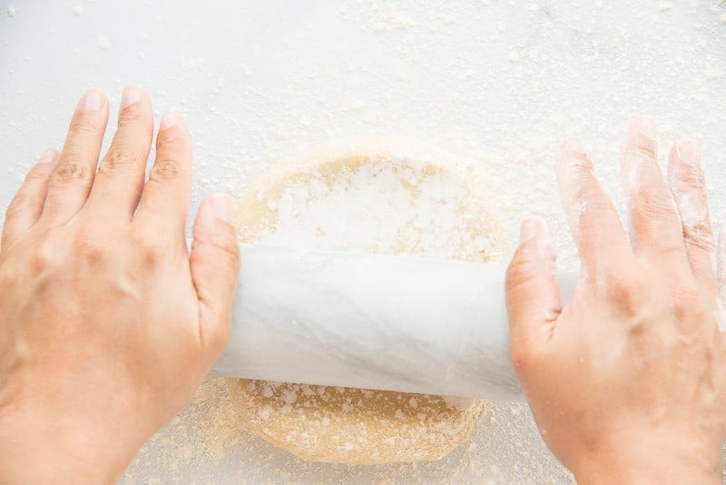 Hands rolling pie dough out with marble rolling pin