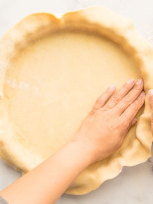 Preview for Flaky Pie Dough hands pressing pie dough into a pie tin before baking.