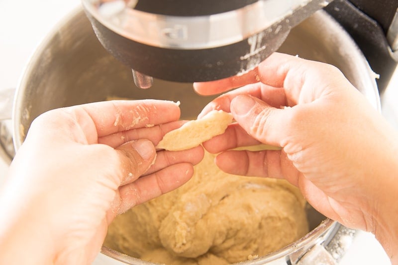 Two hands pull apart a piece of the dough to show it's texture.