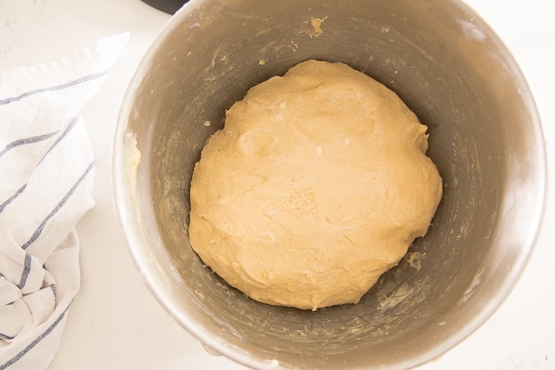 The dough is in a metal mixing bowl next to a blue and white striped kitchen towel.