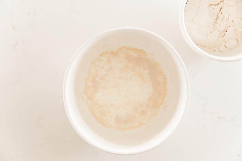 Yeast is added to a white ceramic bowl of milk and honey. Top left: a ceramic bowl of flour