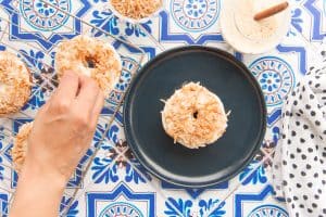 A hand garnishes the donut with coconut flakes