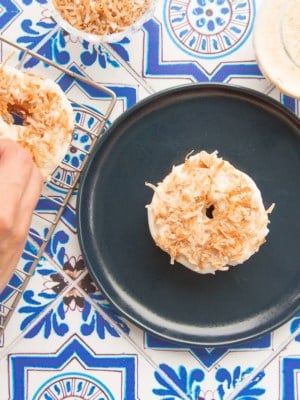 A hand garnishes the donut with coconut flakes