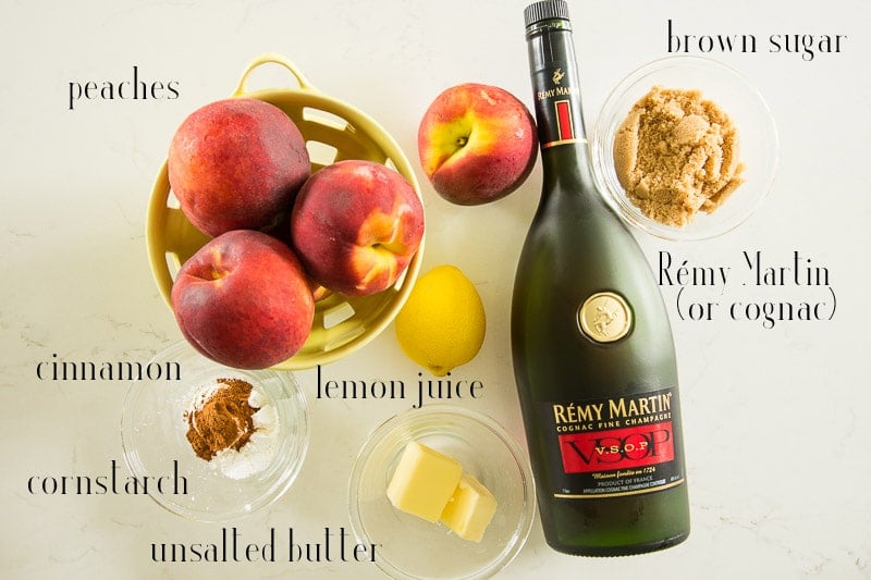 Ingredients to make the Peach-cognac topping on a white surface: peaches, brown sugar, Remy Martin (or cognac), unsalted butter, lemon juice, cinnamon, and cornstarch.