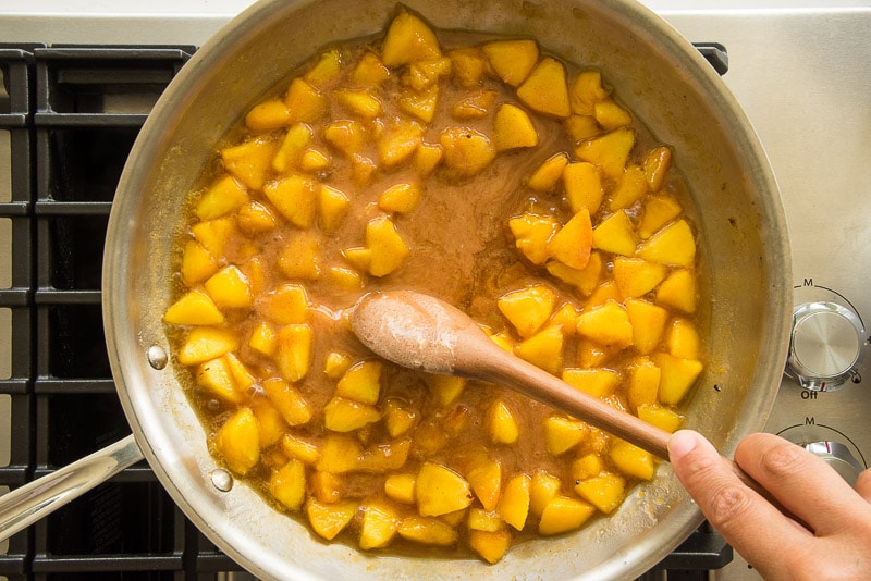 A wooden spoon is used to stir the cornstarch slurry into the pan of peaches.