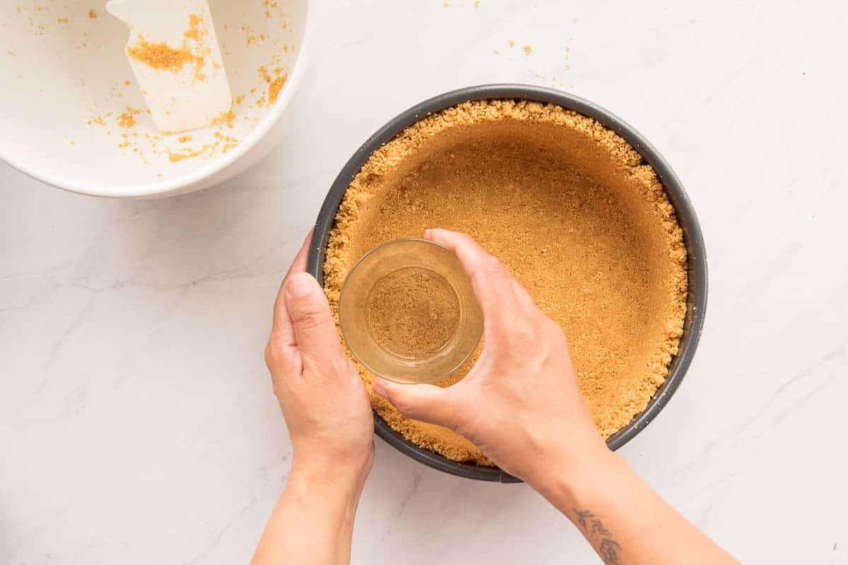 The maria cookie crust is pressed into a springform pan with a glass cup.