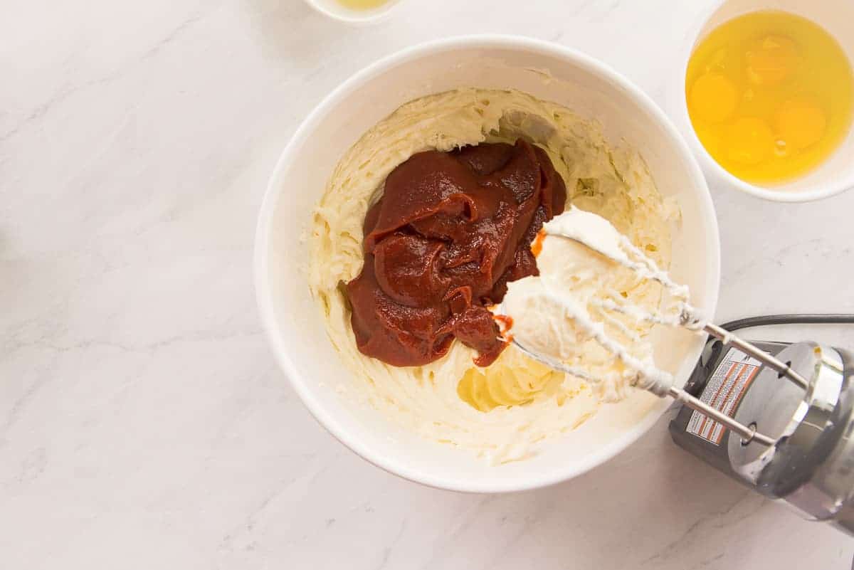 The melted guava paste is added to a white mixing bowl with the cream cheese mixture.