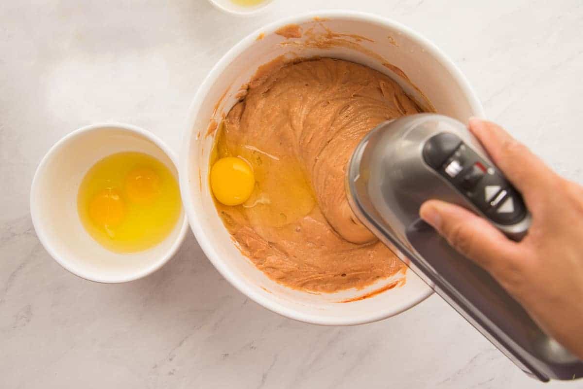 Eggs are added to a white ceramic bowl and blended in with an electric hand mixer